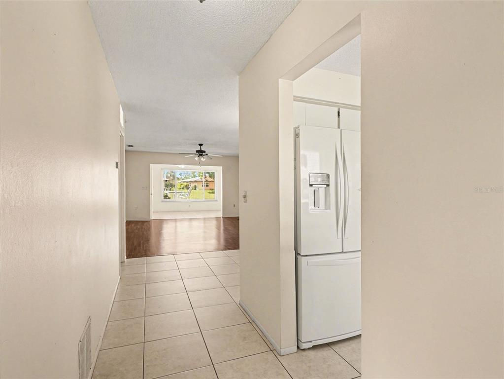 A tiled hallway leads to a living area with wood-look flooring and a white refrigerator — 6608 AUBURN AVENUE, BRADENTON, FL