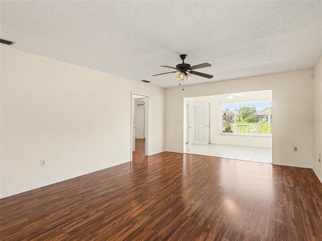 An empty living room features dark wood-look flooring, white walls, and a ceiling fan — 6608 AUBURN AVENUE, BRADENTON, FL