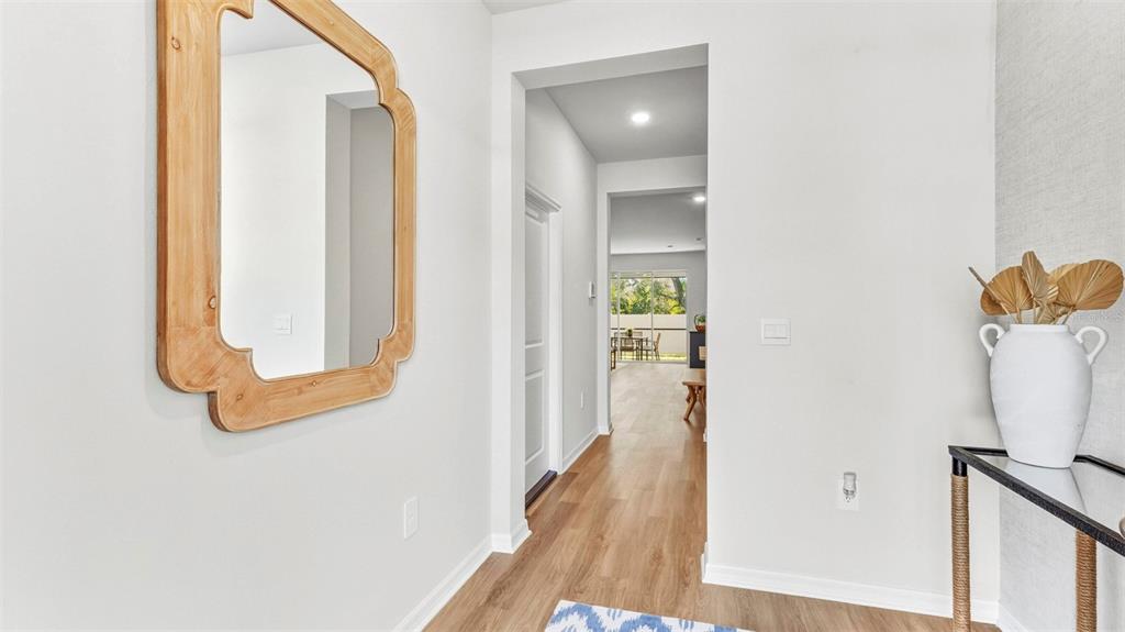 A bright entryway features light wood flooring, a decorative mirror, and a white vase — 4052 GOLD DUST LANE, SARASOTA, FL