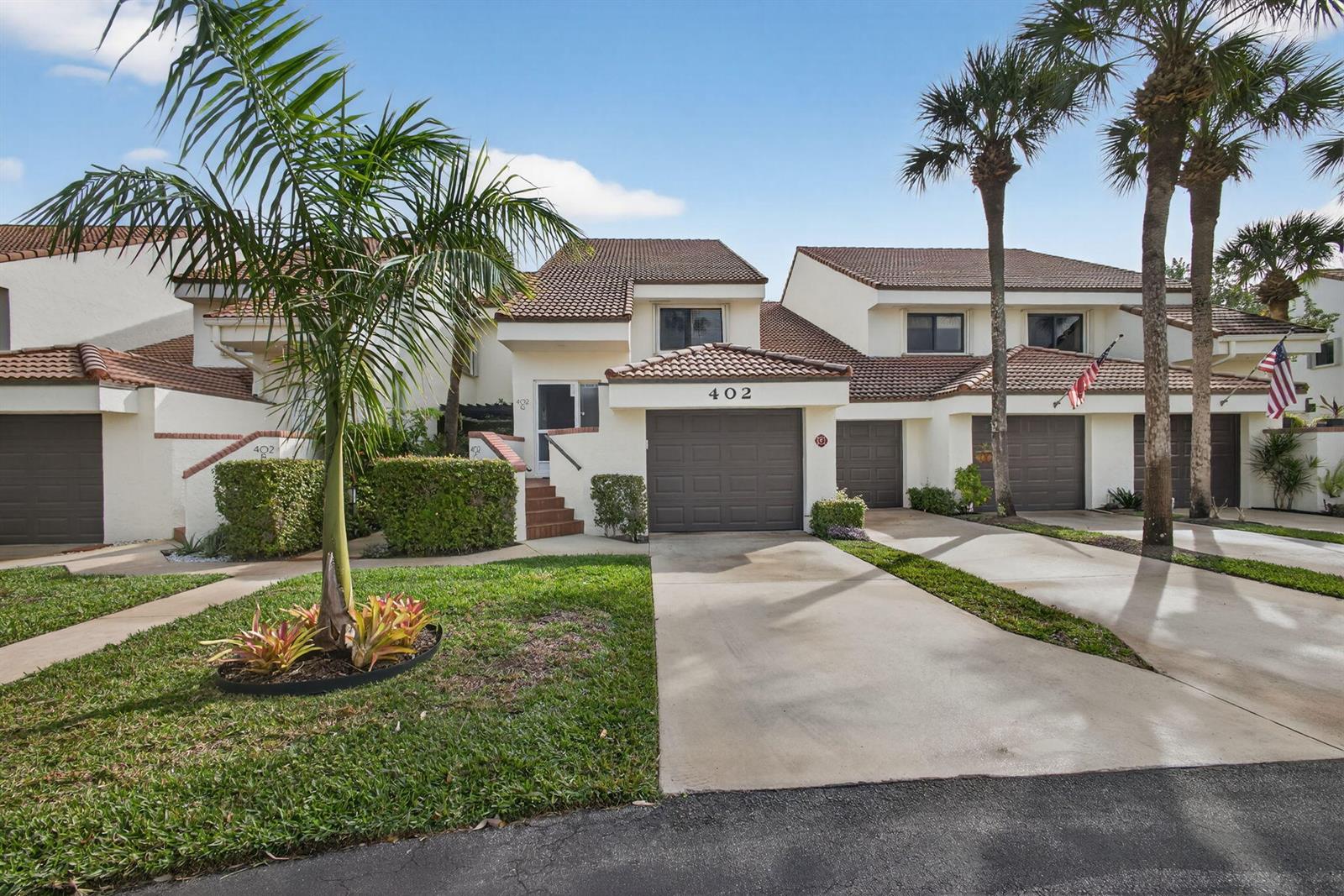 The exterior of a multi-unit residential building features brown garage doors and palm trees — 402 Sea Oats Drive # G, Juno Beach FL 33408, JUNO BEACH, FL