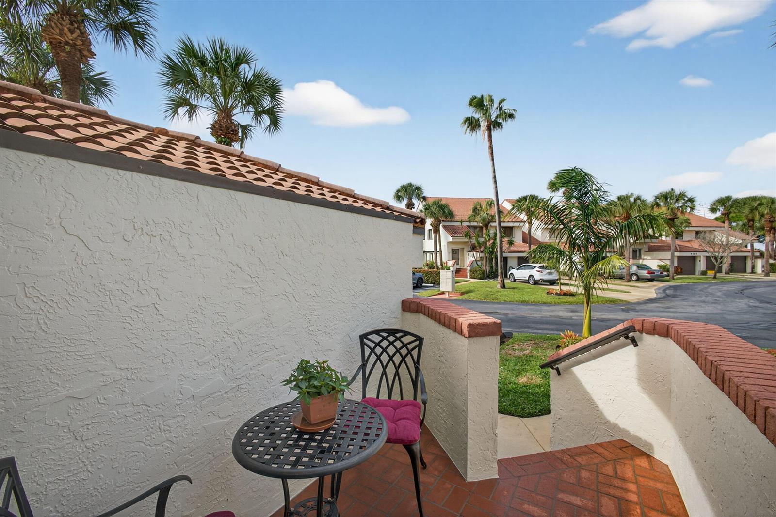 A small patio with a metal table and chair overlooks a residential street with palms — 402 Sea Oats Drive # G, Juno Beach FL 33408, JUNO BEACH, FL