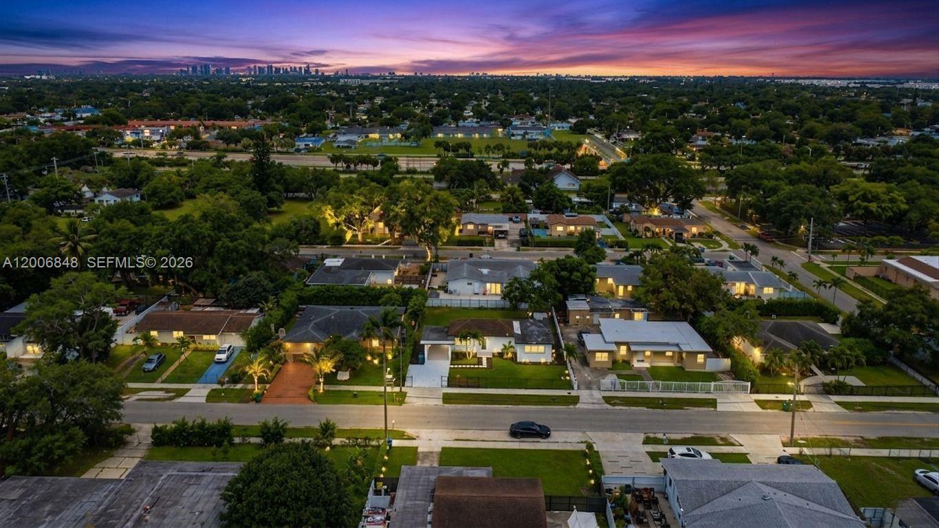 An aerial view shows a suburban neighborhood with houses, green trees, and a sunset sky — 2870 NW 169th Ter, Miami Gardens FL 33056, MIAMI GARDENS, FL