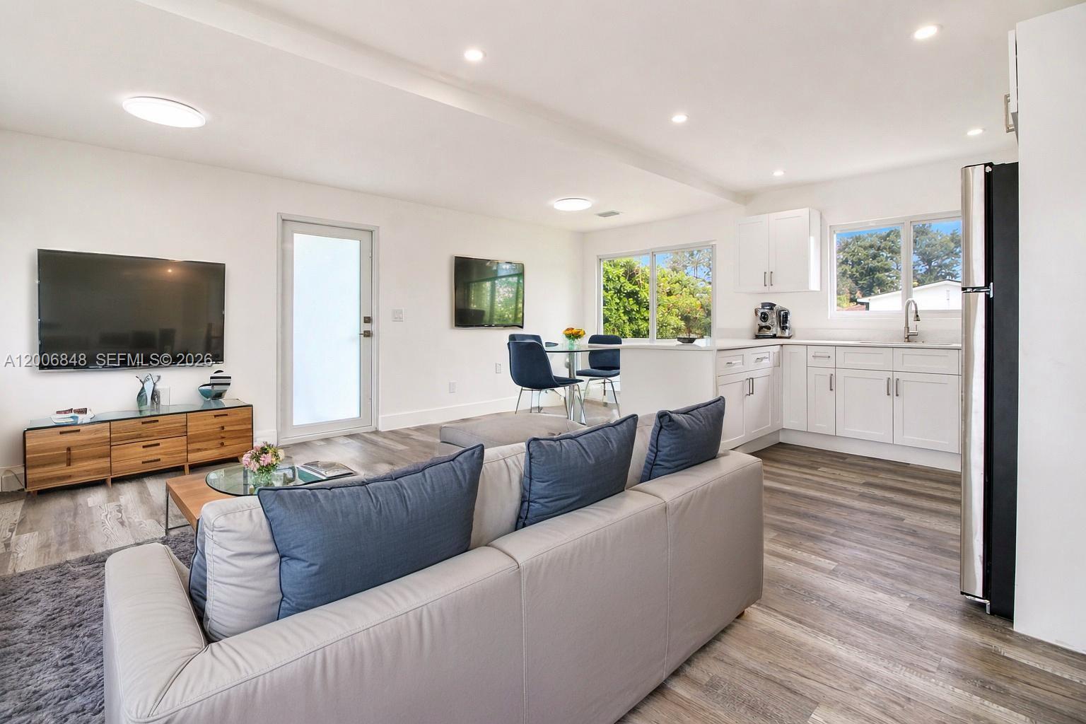 An open-concept living room and kitchen feature white cabinetry, gray flooring, and a gray sofa — 2870 NW 169th Ter, Miami Gardens FL 33056, MIAMI GARDENS, FL