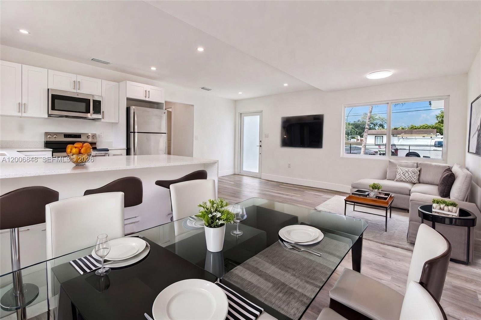 An open-concept kitchen, dining area, and living room feature white cabinetry and modern furniture — 2870 NW 169th Ter, Miami Gardens FL 33056, MIAMI GARDENS, FL