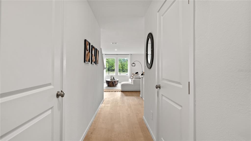 A hallway with light wood flooring leads toward a bright living room with large windows — 3314 WANDEL TERRACE, DAVENPORT, FL