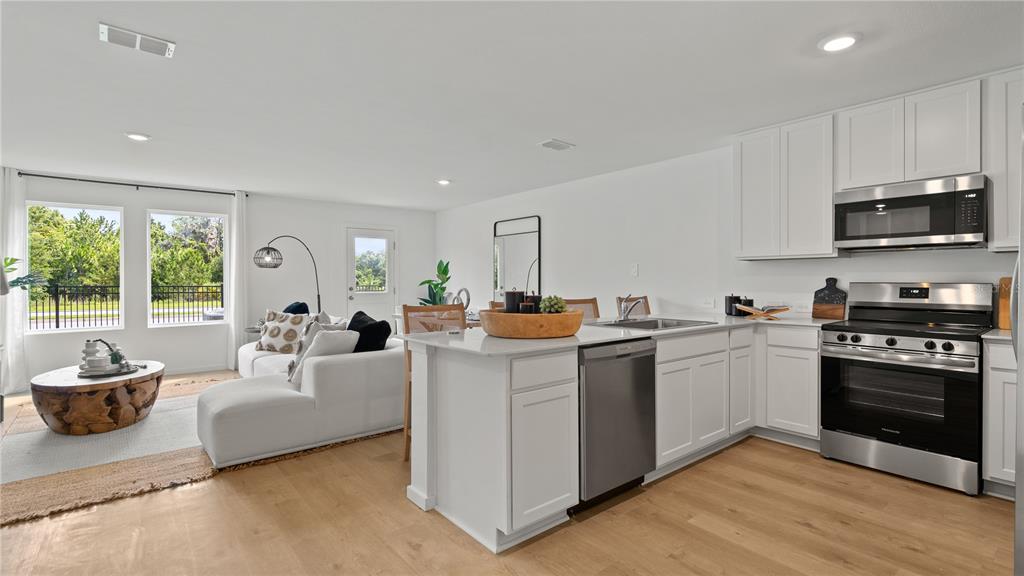 A bright, open-concept kitchen and living area features white cabinetry, stainless steel appliances, and wood-look flooring — 3314 WANDEL TERRACE, DAVENPORT, FL