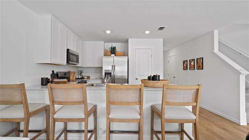 A kitchen features white cabinets, stainless steel appliances, and three wooden bar stools at a counter — 3314 WANDEL TERRACE, DAVENPORT, FL