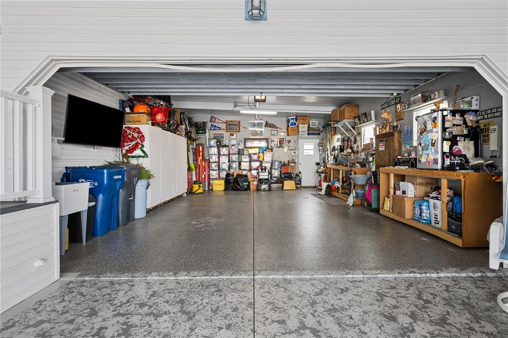 A spacious garage with a speckled concrete floor, storage shelves, a workbench, and a wall-mounted television — 8433 REGAL WAY, PALMETTO, FL