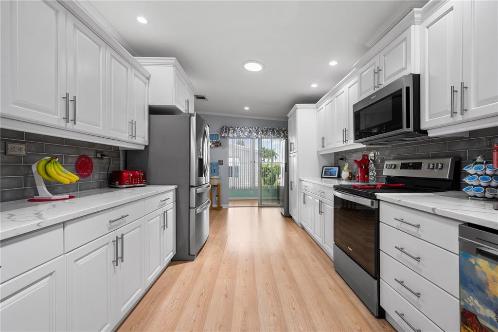 A galley kitchen features white cabinets, stainless steel appliances, gray tile backsplash, and light wood flooring — 8433 REGAL WAY, PALMETTO, FL