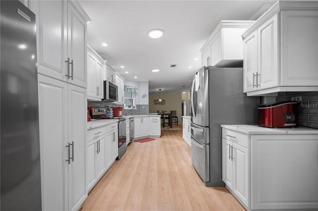 A modern kitchen features white cabinetry, stainless steel appliances, and light wood-look flooring — 8433 REGAL WAY, PALMETTO, FL