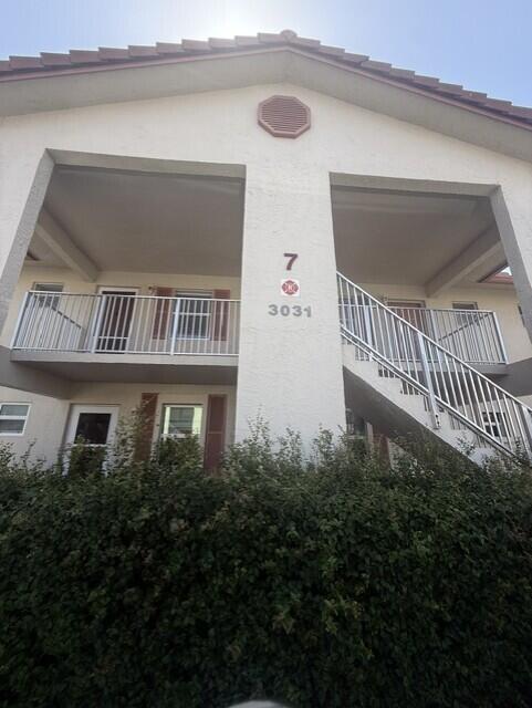 A two-story apartment building exterior features a metal staircase, balconies, and a large hedge — 3031 Holiday Springs Boulevard # 7, Margate FL 33063, MARGATE, FL