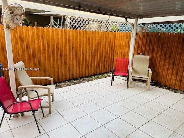 A tiled patio features three outdoor chairs and a wall-mounted fan against a wooden fence — 8075 NW 8th St # 6, Miami FL 33126, MIAMI, FL