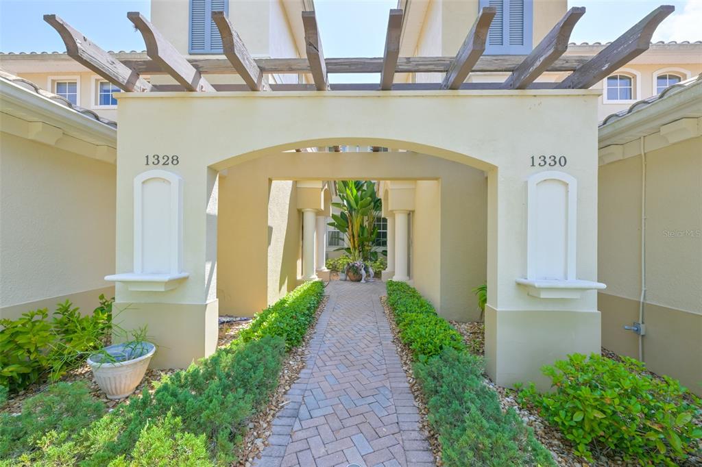 A brick walkway leads through a covered entryway between two building units with address numbers — 1330 EMERALD DUNES DRIVE, SUN CITY CENTER, FL