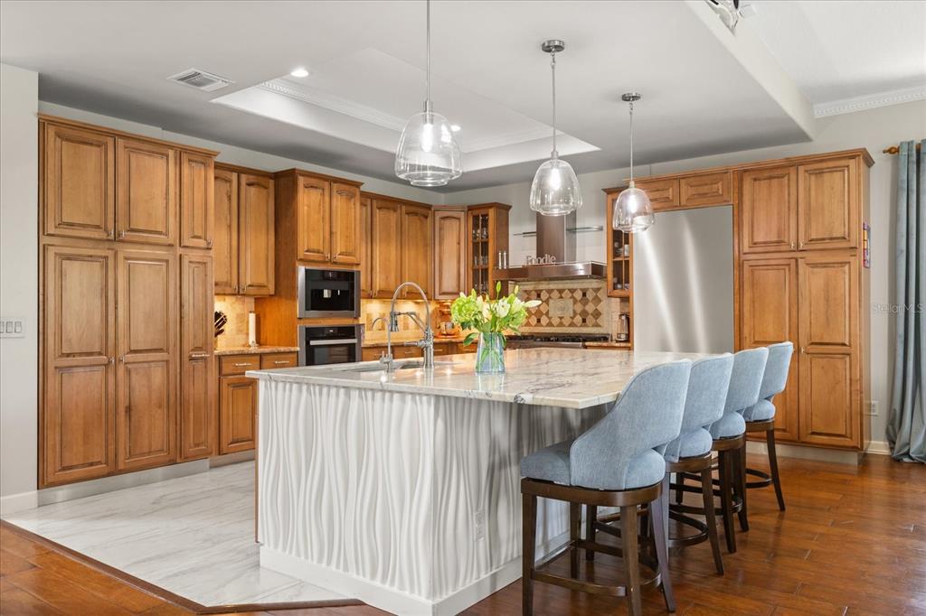 A kitchen features wood cabinets, a white marble-topped island with blue stools, and pendant lighting — 1554 LAKE RHEA DRIVE, WINDERMERE, FL