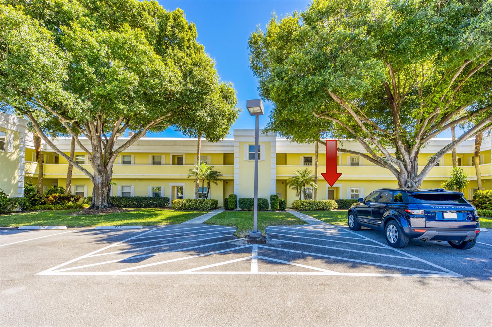 A yellow two-story apartment building with a parking lot and large trees in front — 1600 SE Saint Lucie Boulevard # 205, Stuart FL 34996, STUART, FL