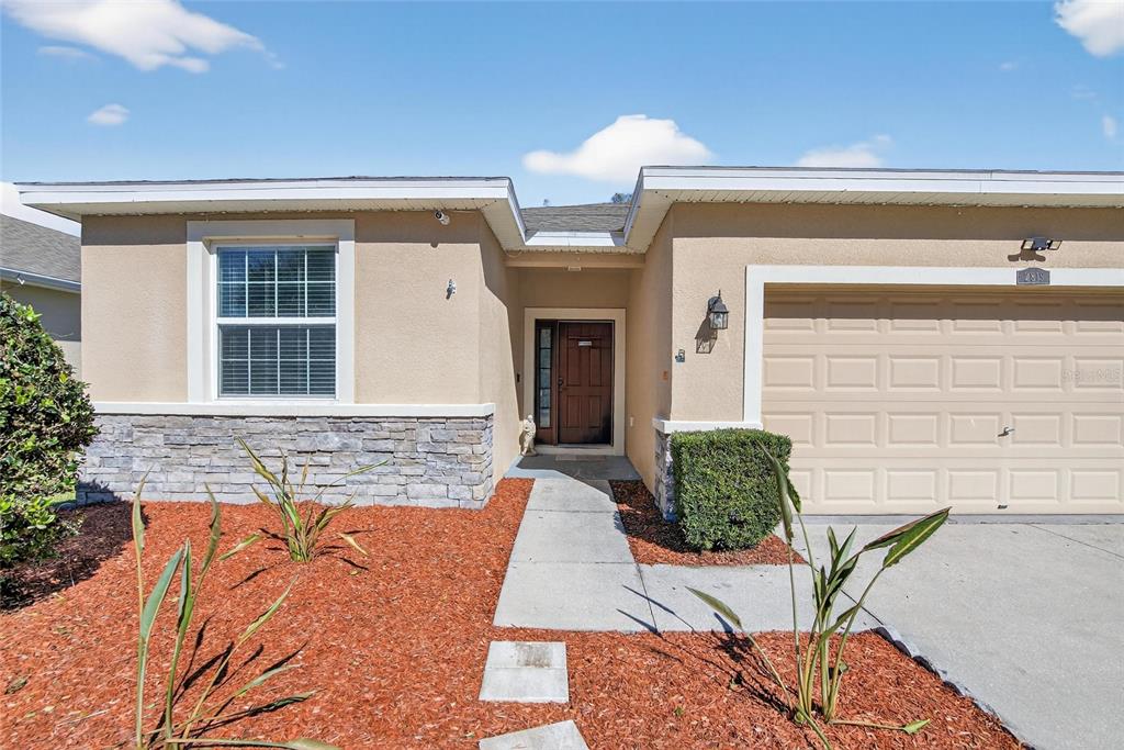 A single-story house exterior features a tan stucco facade, stone accents, and a beige garage — 2819 HOLLY BLUFF COURT, PLANT CITY, FL