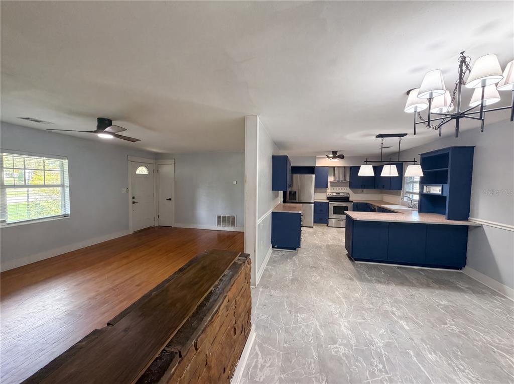 A view of a living room with hardwood floors and an adjacent kitchen with blue cabinets — 820 E WISCONSIN AVENUE, DELAND, FL