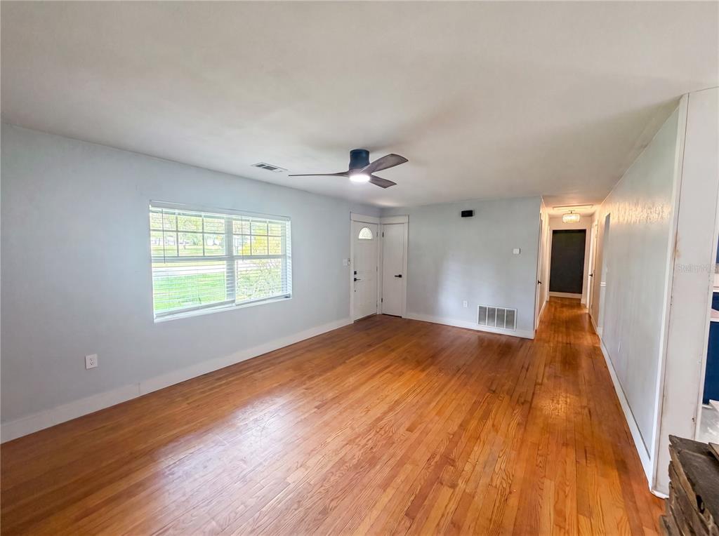 A living room features light blue walls, hardwood floors, a ceiling fan, and a window — 820 E WISCONSIN AVENUE, DELAND, FL