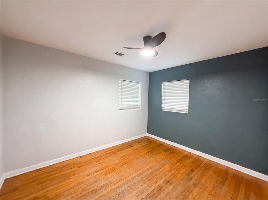 An empty bedroom features hardwood floors, a ceiling fan, and a dark blue accent wall — 820 E WISCONSIN AVENUE, DELAND, FL