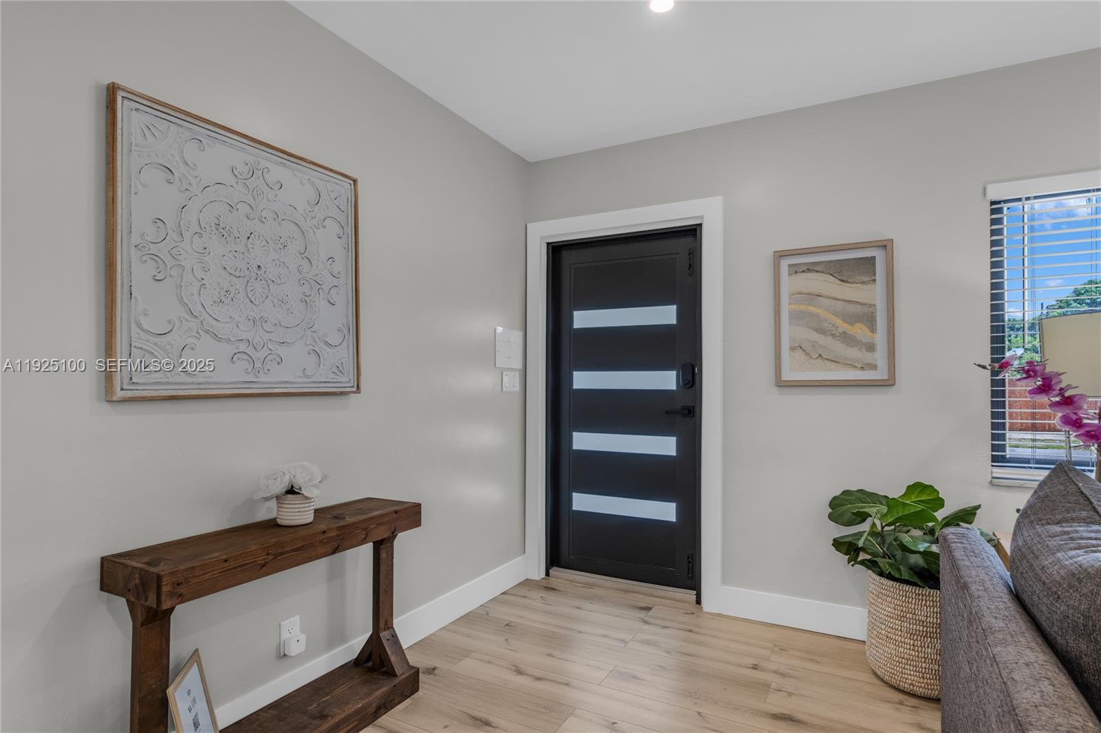 An entryway features a dark modern door, a wooden console table, and light wood flooring — 1204 NE 7th St, Pompano Beach FL 33060, POMPANO BEACH, FL