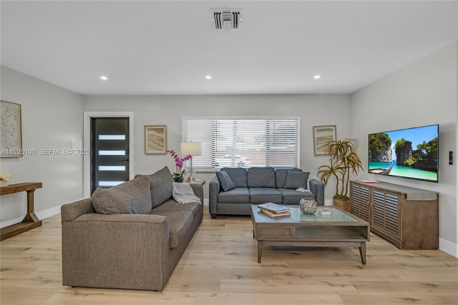 A living room features two gray sofas, a coffee table, and a wall-mounted television — 1204 NE 7th St, Pompano Beach FL 33060, POMPANO BEACH, FL