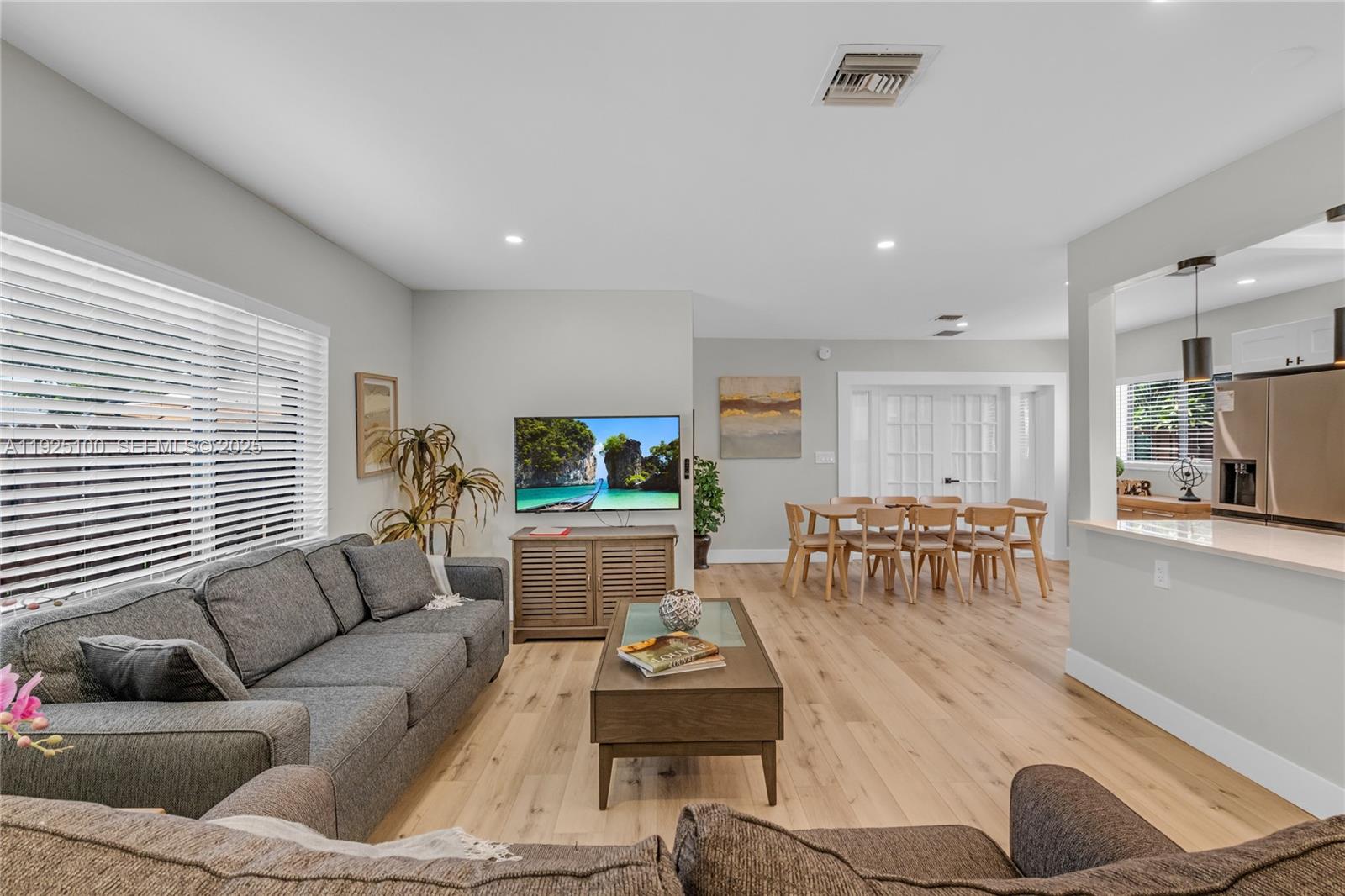 A living room and dining area feature light wood flooring, gray furniture, and white walls — 1204 NE 7th St, Pompano Beach FL 33060, POMPANO BEACH, FL