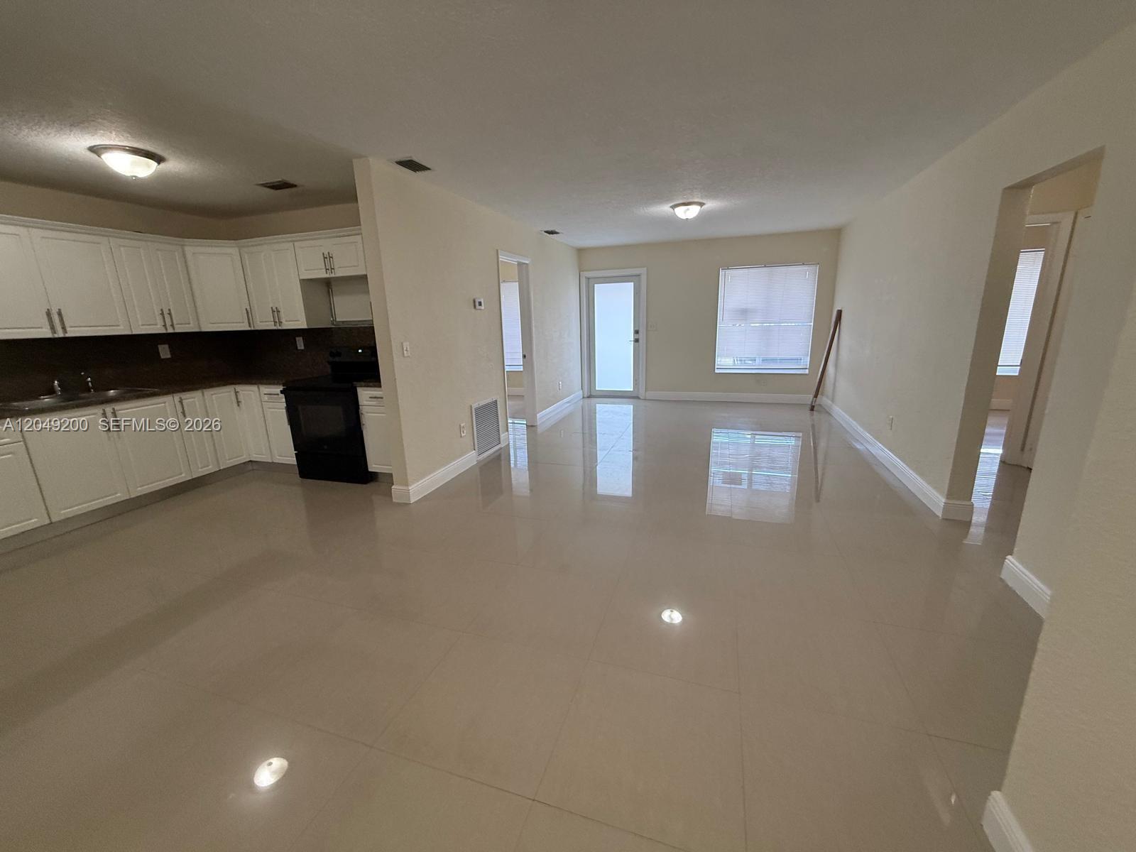 An open-concept room features large beige floor tiles, light-colored walls, and an adjacent kitchen — 4309 SW 129th Ave, Miami FL 33175, MIAMI, FL