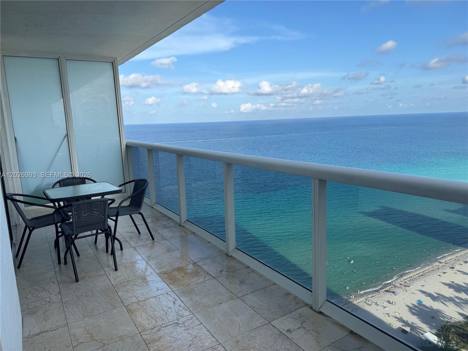 A balcony with a glass railing overlooks the ocean and a sandy beach below — 1830 S Ocean Dr # 3003, Hallandale Beach FL 33009, HALLANDALE BEACH, FL