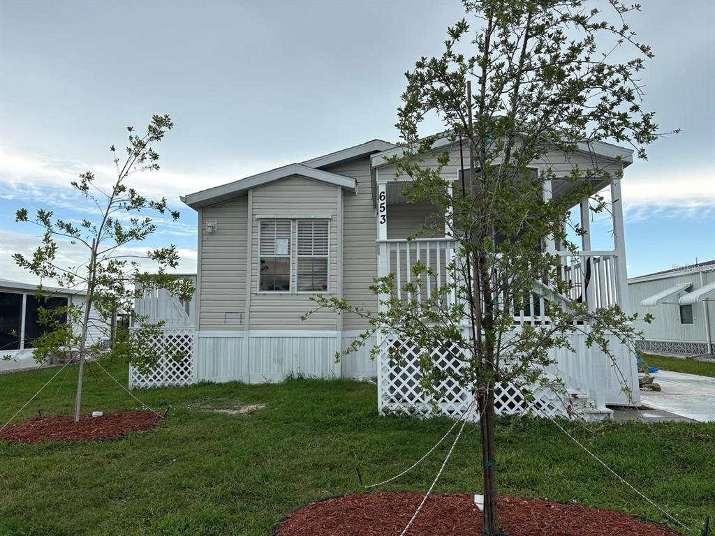 A light-colored manufactured home features a front porch, lattice skirting, and two young trees — 653 LOS ALTOS, NORTH PORT, FL