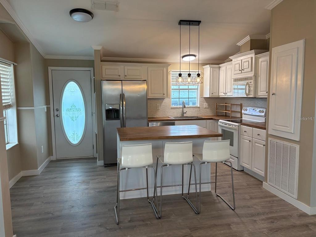 A kitchen features white cabinets, stainless steel appliances, a wood-topped island, and three bar stools — 653 LOS ALTOS, NORTH PORT, FL