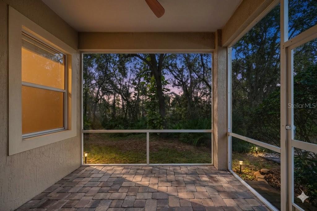A screened-in patio features paver flooring and a view of trees at dusk — 4759 LATHLOA LOOP, LAKELAND, FL
