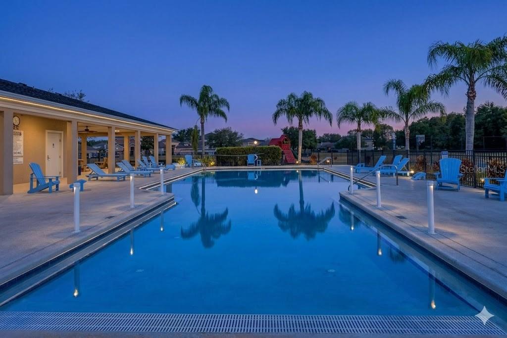 A swimming pool with lounge chairs sits in front of a covered patio at dusk — 4759 LATHLOA LOOP, LAKELAND, FL