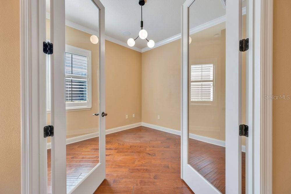 A view through French doors into an empty room with hardwood floors and a light fixture — 4759 LATHLOA LOOP, LAKELAND, FL