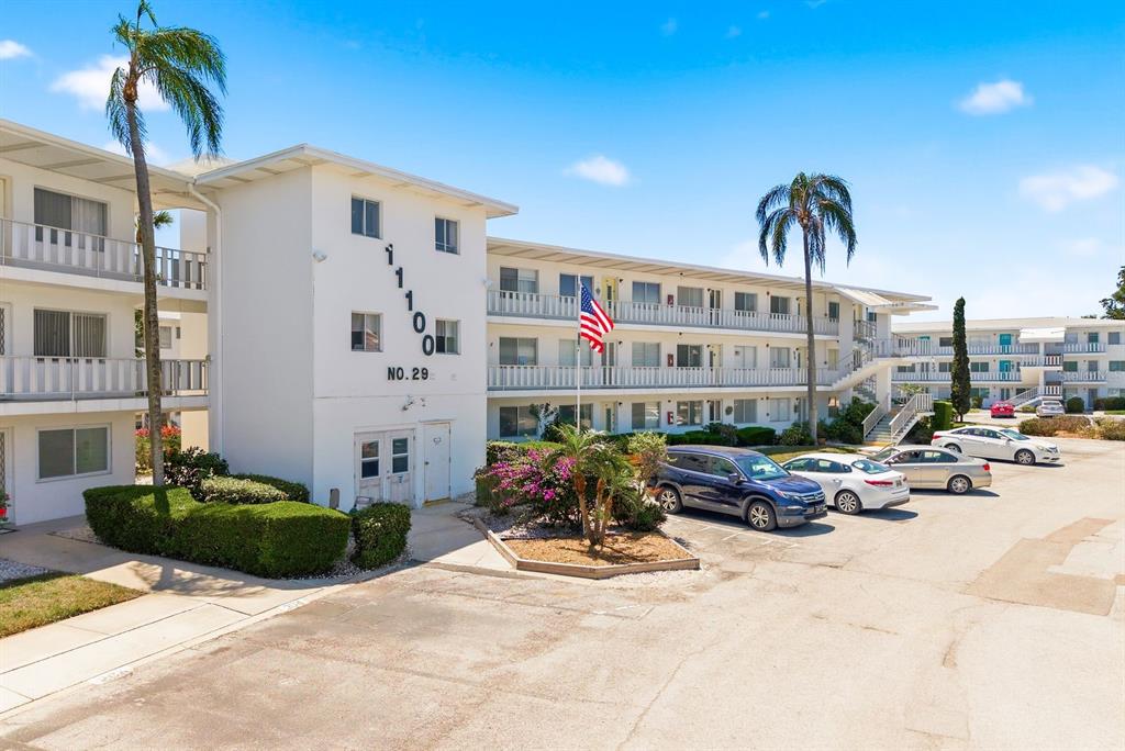 A multi-story white apartment building features a parking lot and palm trees outside — 11100 86TH AVENUE UNIT 310, SEMINOLE, FL