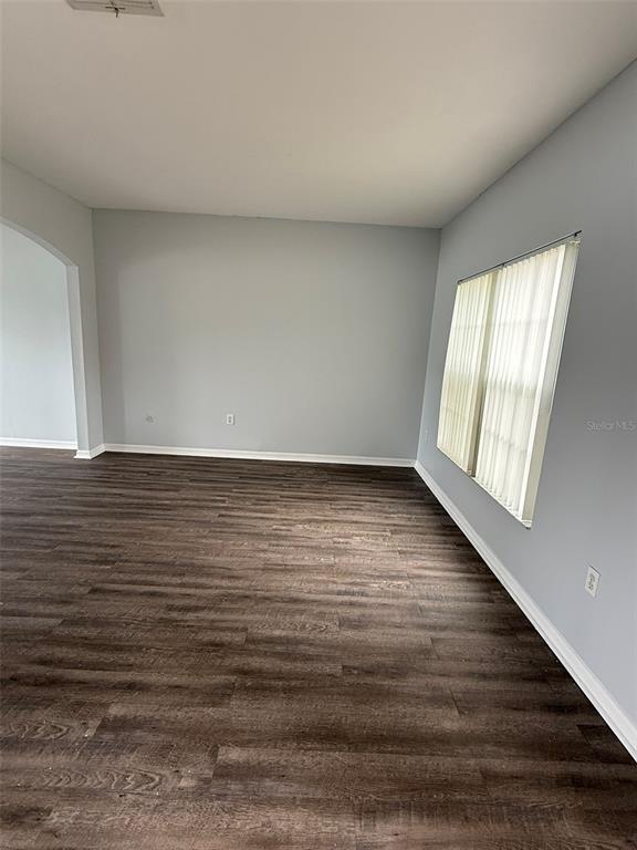 An empty room features light gray walls, dark wood-look flooring, and a window with blinds — 1117 CAMBOURNE DRIVE, KISSIMMEE, FL