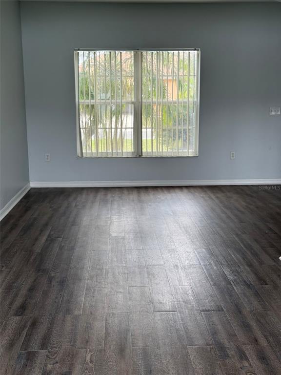 An empty room features light blue walls, dark wood-look flooring, and a large window with blinds — 1117 CAMBOURNE DRIVE, KISSIMMEE, FL