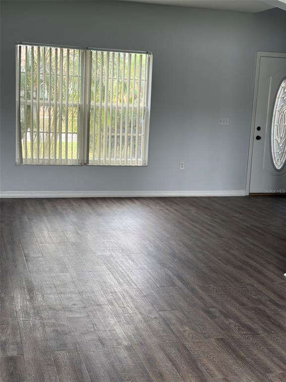 A room with light gray walls, dark wood-look flooring, vertical blinds, and a white door — 1117 CAMBOURNE DRIVE, KISSIMMEE, FL