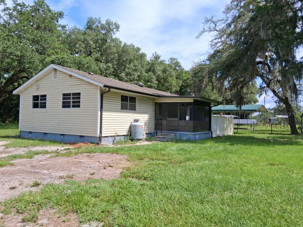 A light-yellow, single-story house with a screened-in porch sits on a grassy, tree-filled lot — 10628 CR 771, WEBSTER, FL