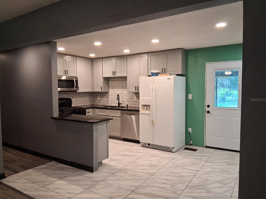 A kitchen with grey cabinets, stainless steel appliances, white subway tile, and light tiled flooring — 10628 CR 771, WEBSTER, FL