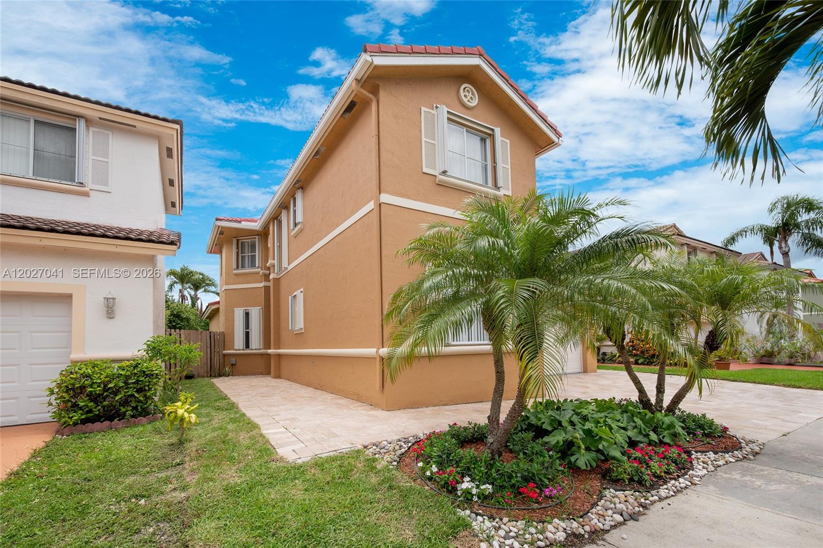 A two-story tan stucco house features a paved driveway, palm trees, and a small garden — 15558 SW 112th Dr, Miami FL 33196, MIAMI, FL