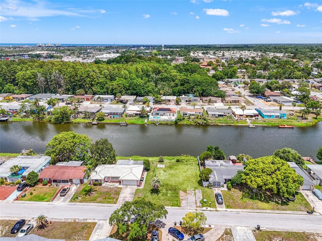 An aerial view shows a vacant residential lot situated between two houses along a canal — 7211 ASHWOOD DRIVE, PORT RICHEY, FL