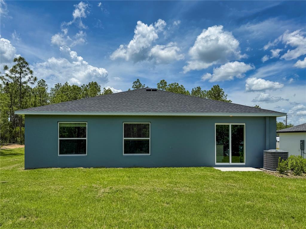 The rear exterior of a gray, single-story house features two windows and a sliding door — 13145 SW 83RD TERR ROAD, OCALA, FL
