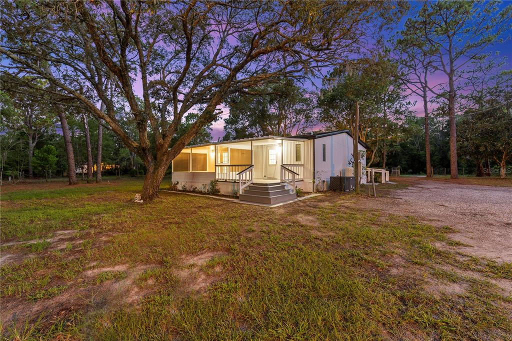 A mobile home with a screened-in porch sits on a grassy lot with large trees — 17544 GALVESTON STREET, SPRING HILL, FL