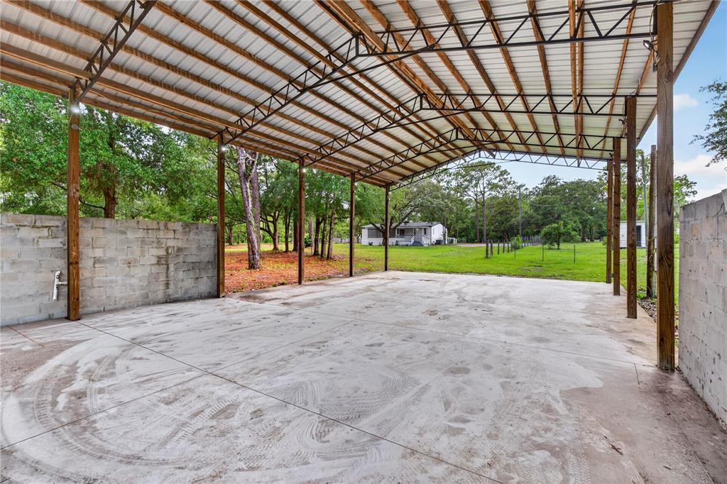 A large, open-air metal carport with a concrete floor and partial cinder block walls — 17544 GALVESTON STREET, SPRING HILL, FL