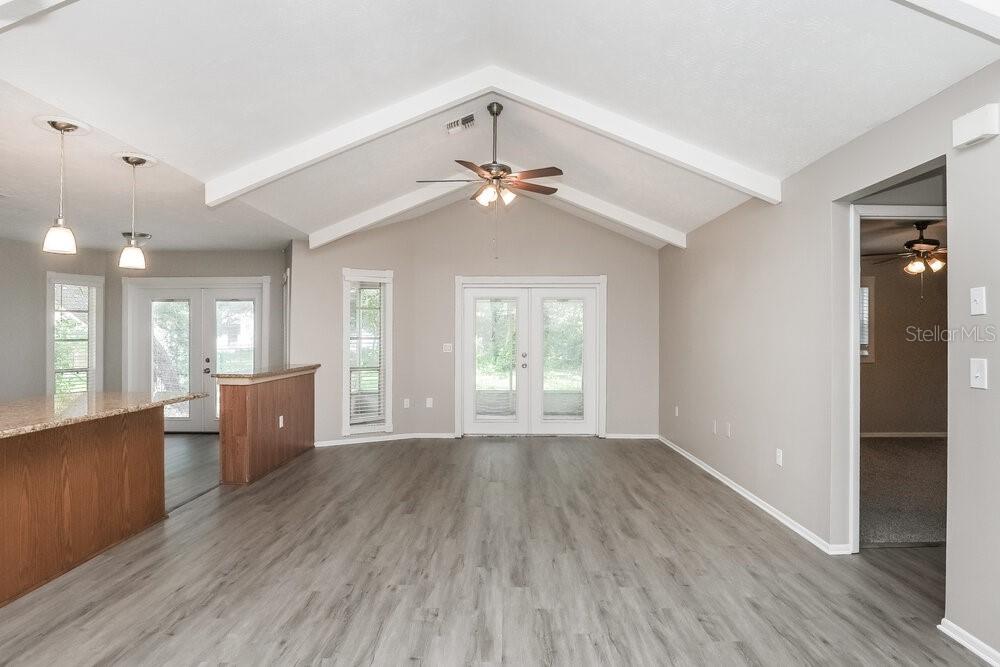 A living room with vaulted ceilings, light wood-look flooring, and glass double doors — 13403 WOODWARD DRIVE, HUDSON, FL