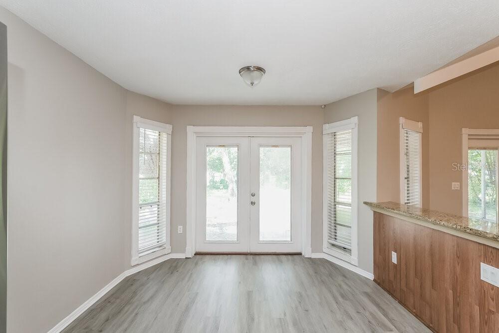 A dining area features light wood-look flooring, beige walls, and double glass doors leading outside — 13403 WOODWARD DRIVE, HUDSON, FL