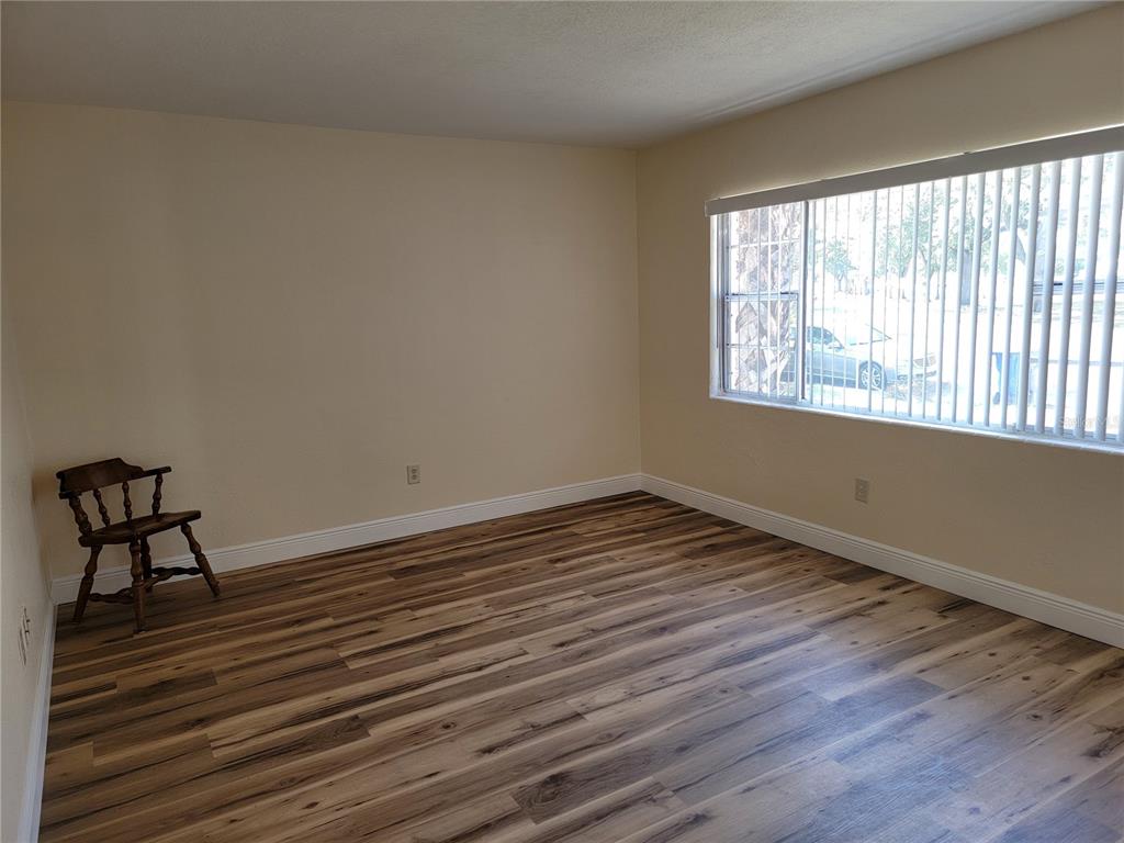 An empty room features light-colored walls, wood-look flooring, and a large window with vertical blinds — 542 & 540 S CLAYTON AVENUE, LAKELAND, FL