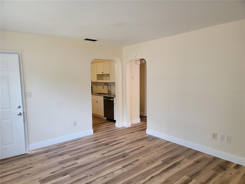 An interior view shows a living area with wood-look flooring leading to an arched kitchen entrance — 542 & 540 S CLAYTON AVENUE, LAKELAND, FL