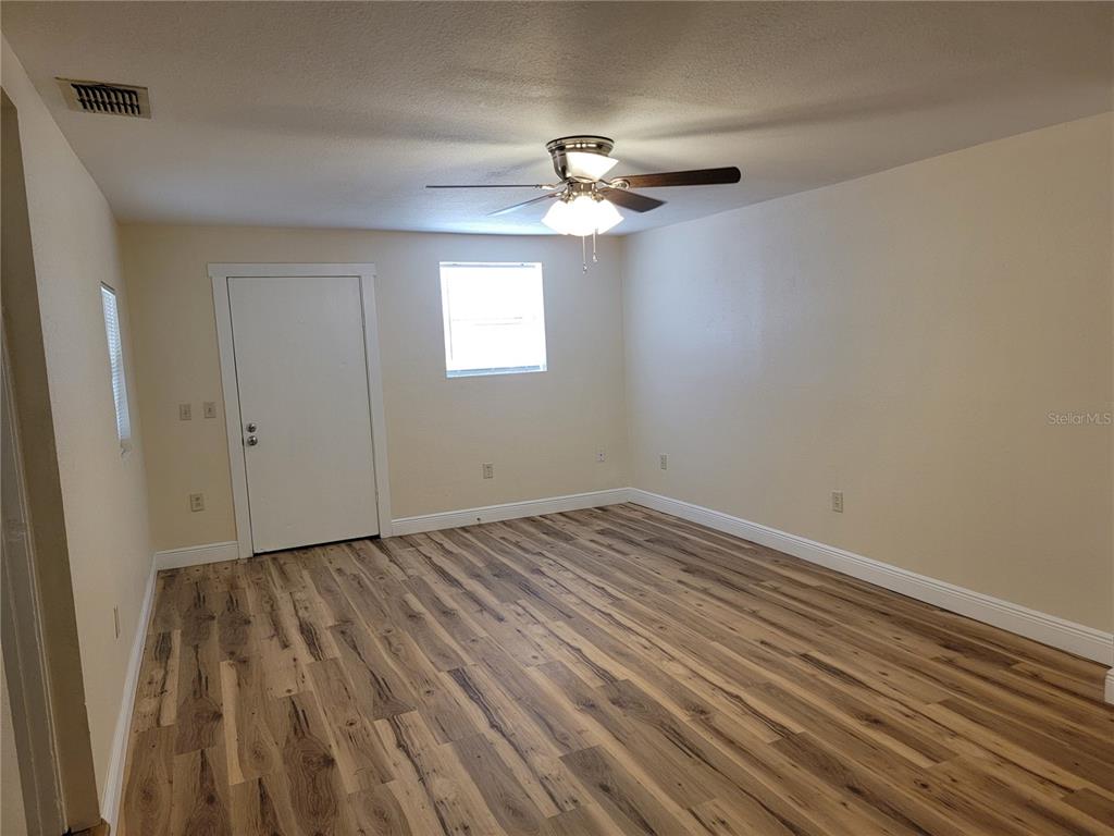 An empty room features light-colored walls, wood-look flooring, a ceiling fan, and a white door — 542 & 540 S CLAYTON AVENUE, LAKELAND, FL
