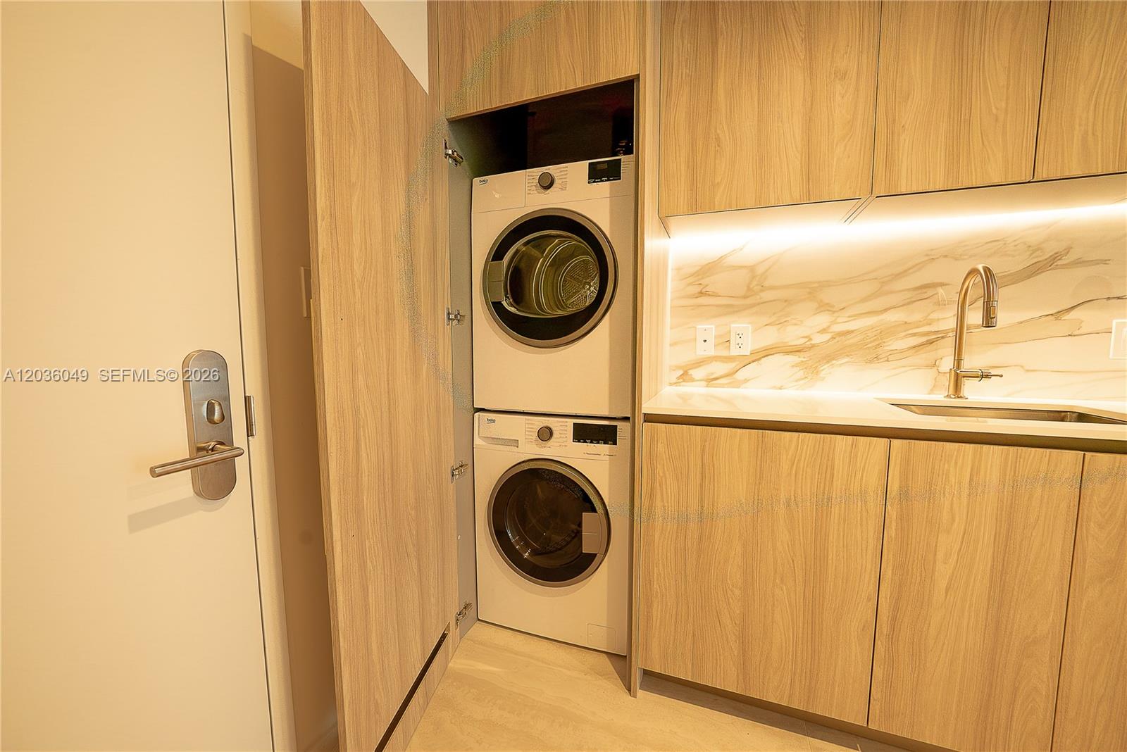 A stacked washer and dryer are built into a kitchen cabinet with light wood cabinetry — 77 SE 5TH ST # 1607, Miami FL 33131, MIAMI, FL